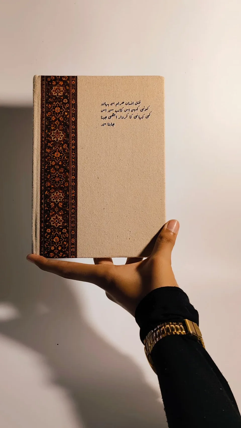 Kaatib diary held in one hand, Urdu couplet on a canvas cover with a Persian carpet panel